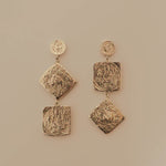 Pair of silver earrings with textured square designs on a beige background