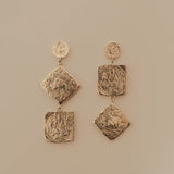 Pair of silver earrings with textured square designs on a beige background