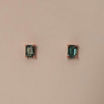 A pair of emerald cut sapphire stud earrings set in 9ct rose gold, displayed against a pink background.