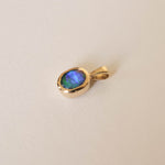 A gold pendant with an oval-shaped iridescent blue-green opal gemstone, shown on a plain off-white background.