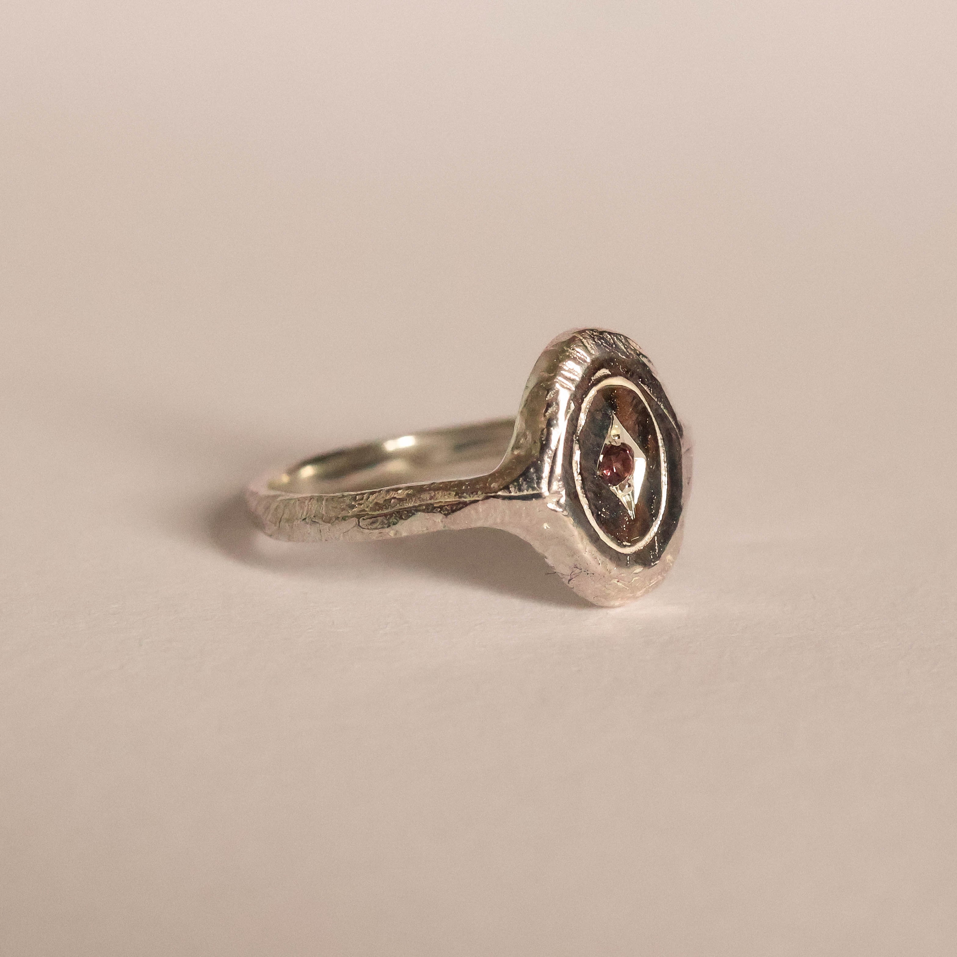 Silver ring with a red gemstone on a beige background