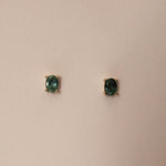 A pair of oval cut sapphire stud earrings set in gold, displayed against a neutral background.