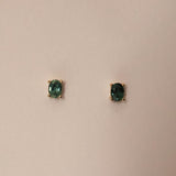 A pair of oval cut sapphire stud earrings set in gold, displayed against a neutral background.
