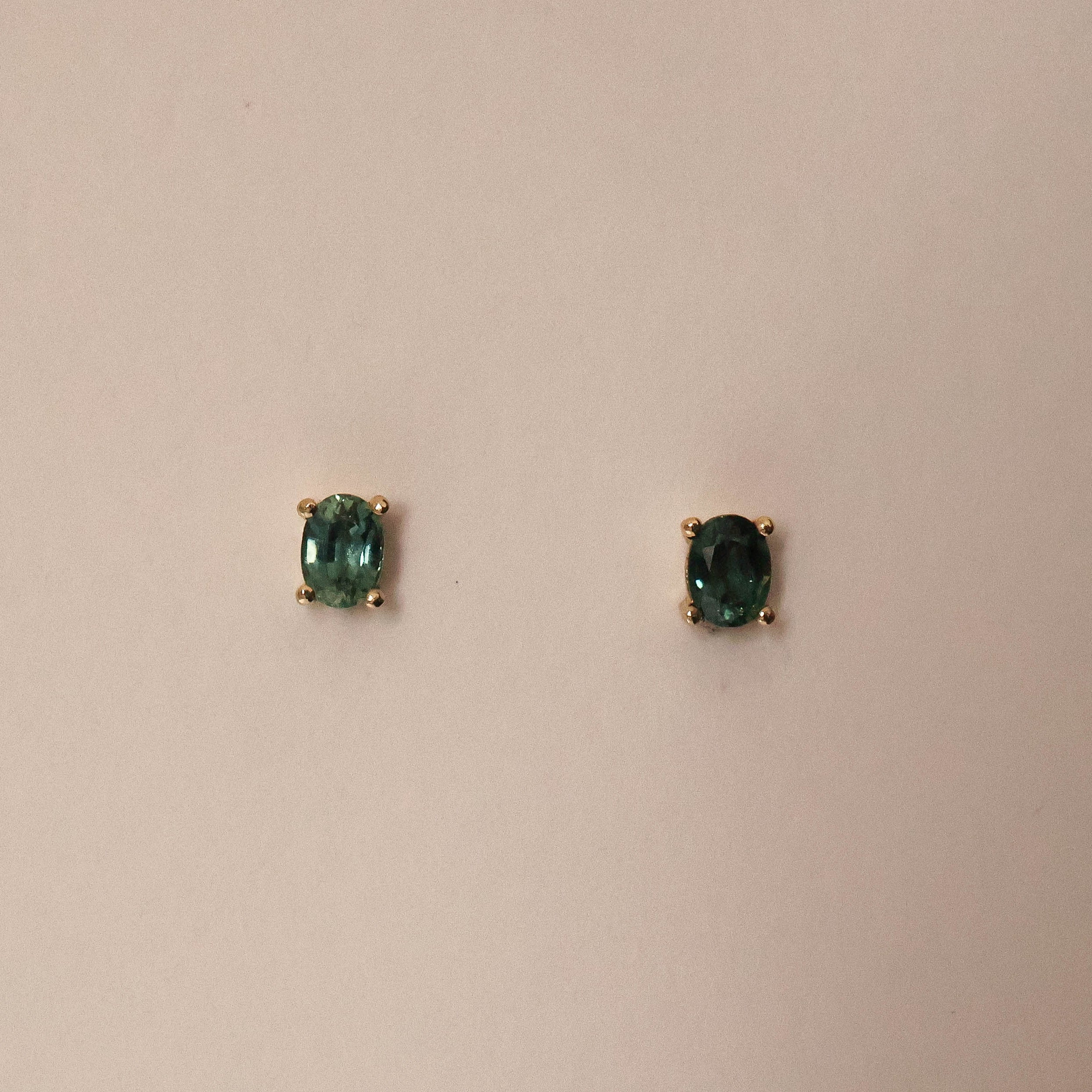 A pair of oval cut sapphire stud earrings set in gold, displayed against a neutral background.