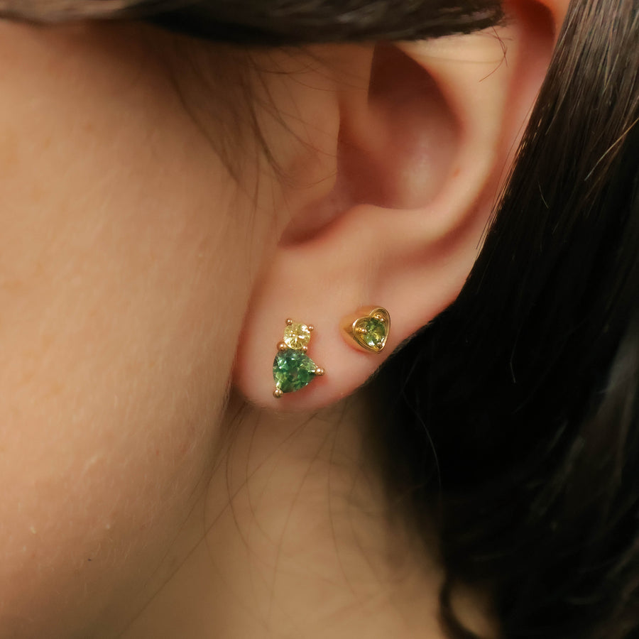 Close-up of an ear wearing gold earrings with green gemstones.